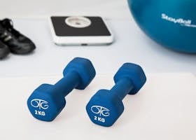physiotherapy-weight-training-dumbbell-exercise-balls-39671-39671 Blue dumbbells placed on a white surface with fitness equipment in the background.